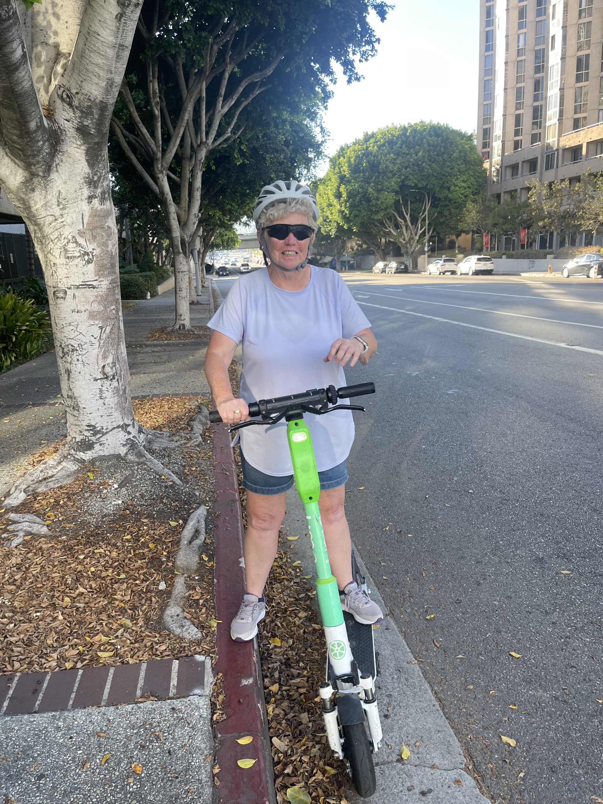 Joan standing with a rented e-scooter on a city sidewalk, wearing a helmet